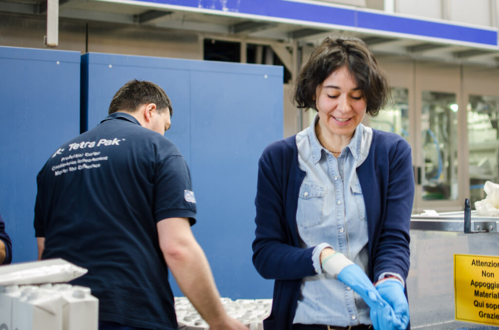 Ragazzo e ragazza durante il turno di lavoro in tetrapak per il servizio Diversity Management di Coopattiva. La ragazza e intenta a togliersi i guanti mentre il ragazzo è di spalle.