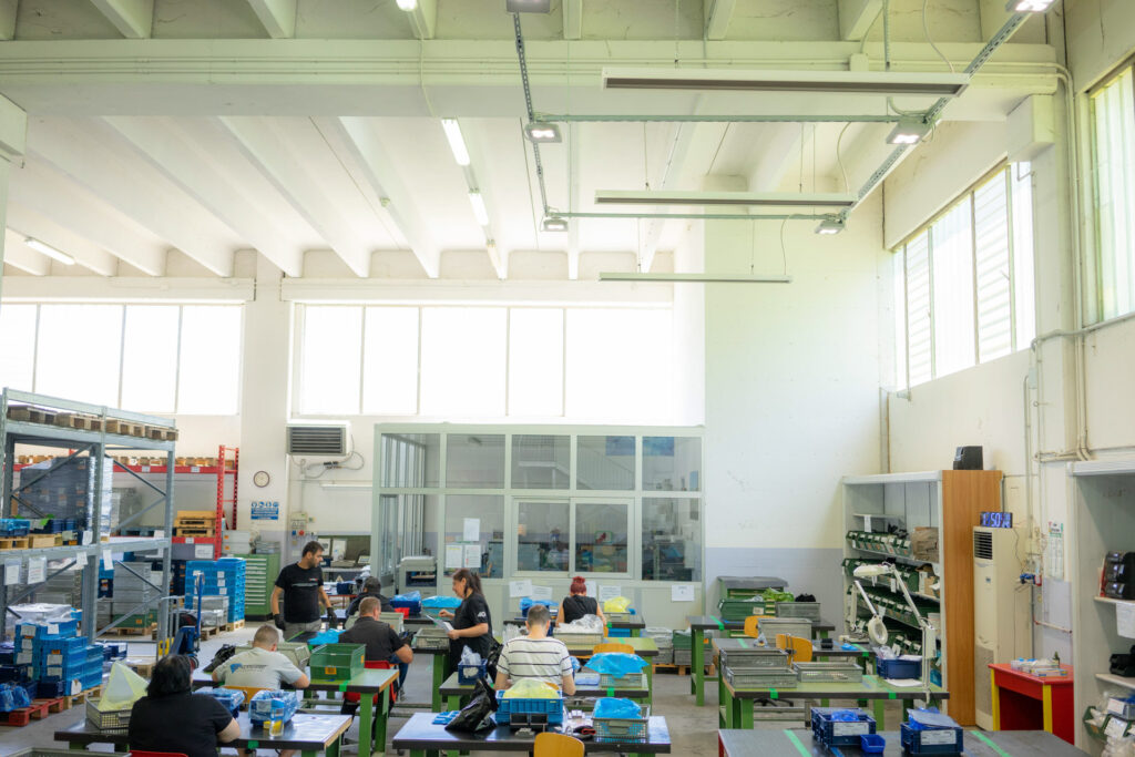 Veduta di lato dell'interno del laboratorio socio occupazionale coopattiva di frignano. Si vedono uomini e donne impegnati durante le lavorazioni.