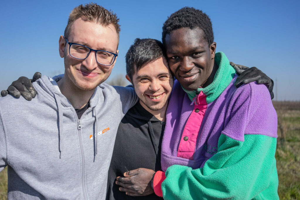 3 ragazzi felici che sorridono in un campo natura che cura di coopattiva