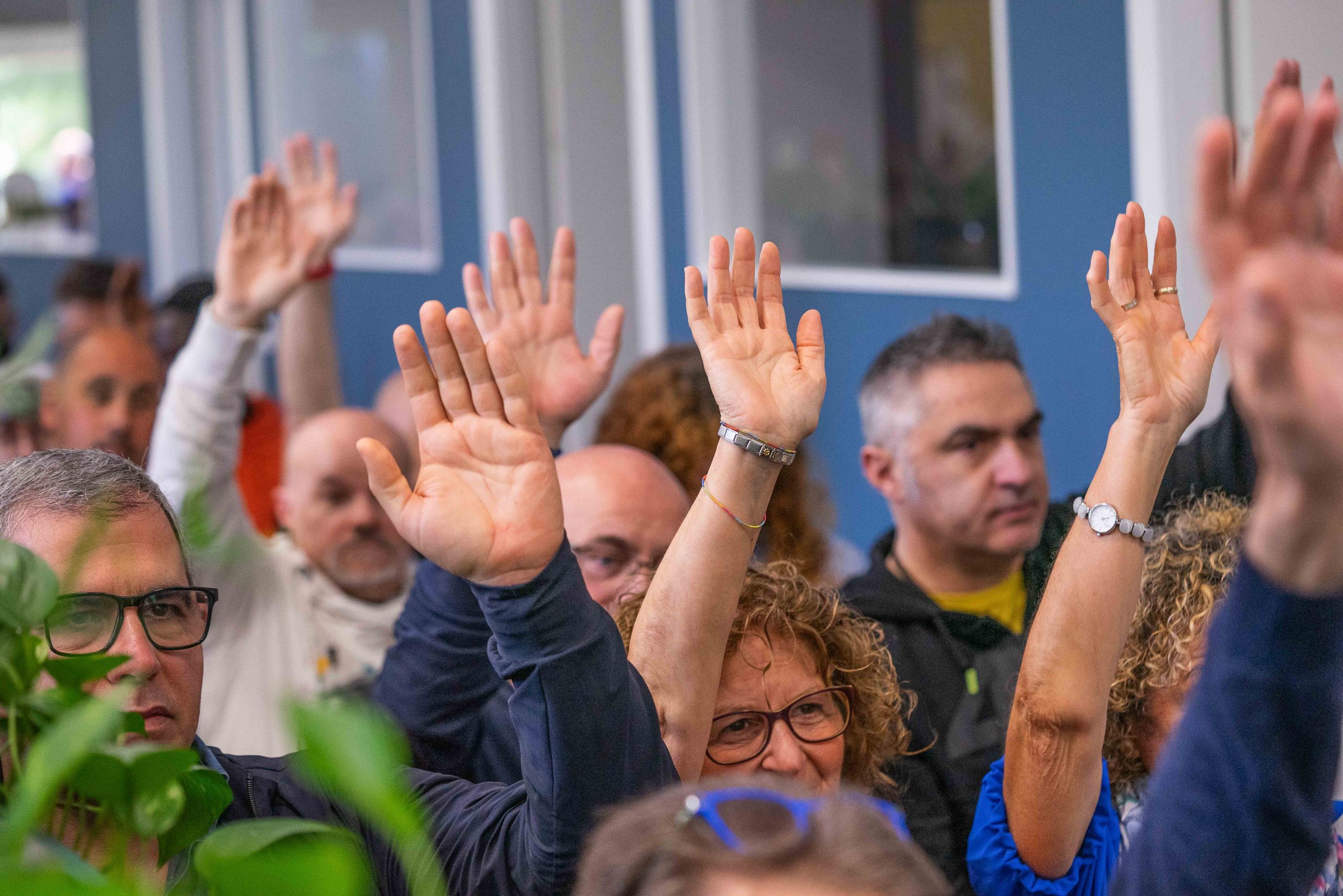 Persone in gruppo che alzano la mano durante riunione coopattiva